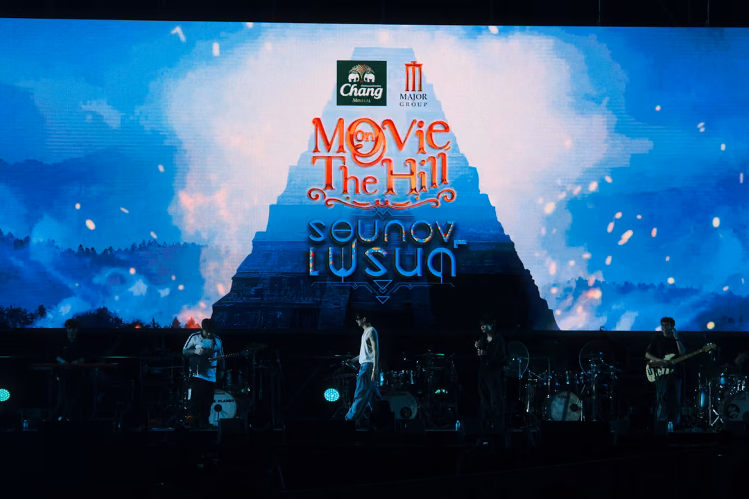 Screen with the Movie on The Hill title over a pyramid and clouds, band members standing on the dim stage below.
