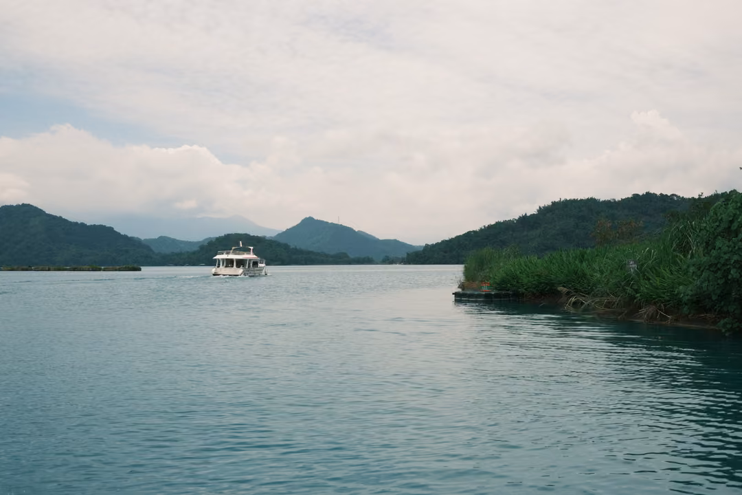 White boat crossing a calm grey-green lake toward a gap between forested hills and distant mountains