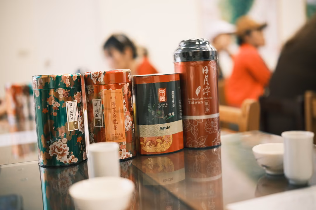 Four decorated tea tins in green, orange, dark green and red on a reflective table with white cups