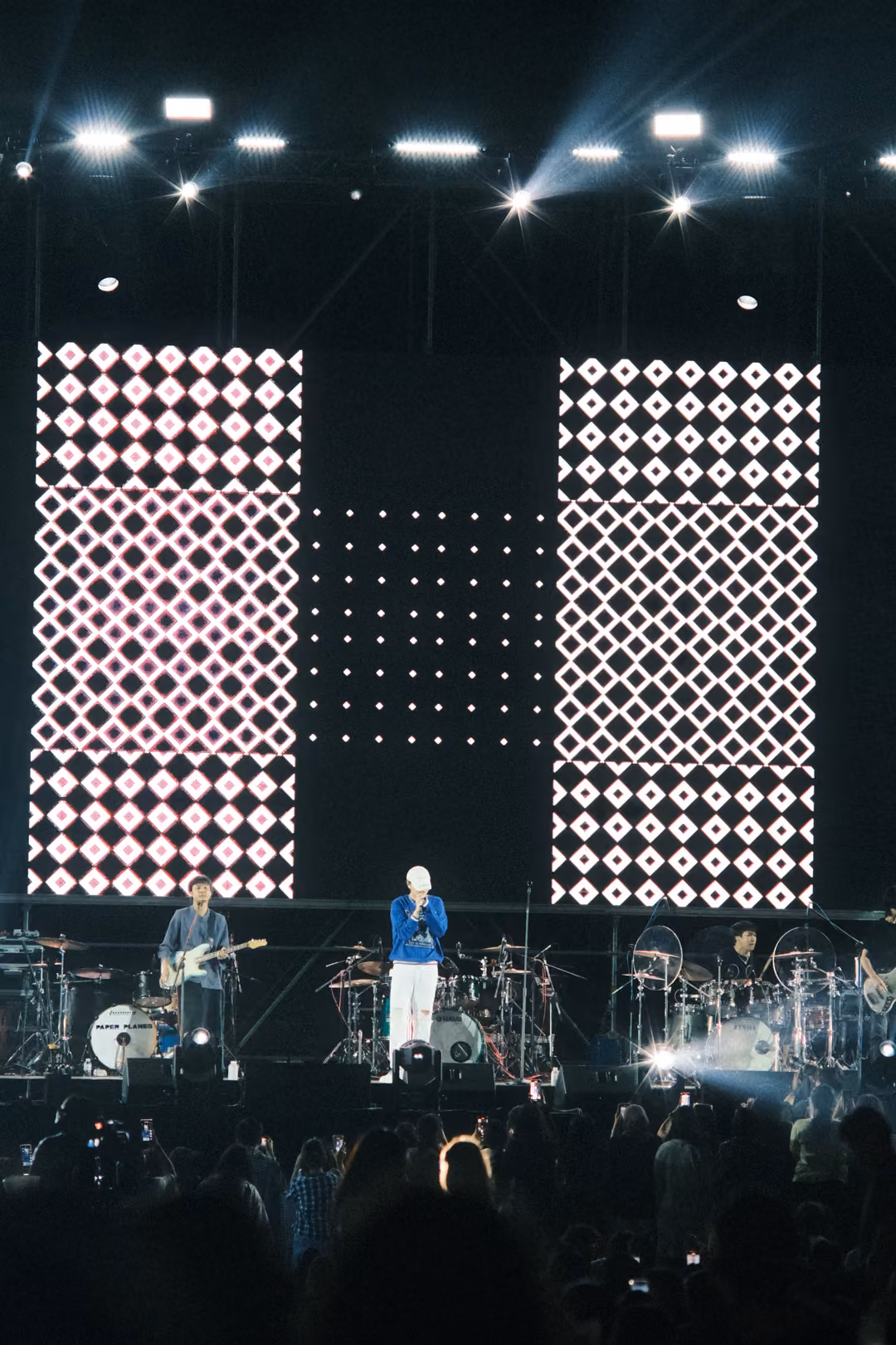 Vertical view of two columns of white diamond patterns on screen, the singer in a blue jacket and guitarist below.