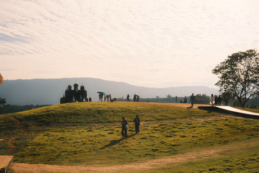 A grassy hilltop with a dark, turreted structure and scattered visitors, mountains under a mottled sky.