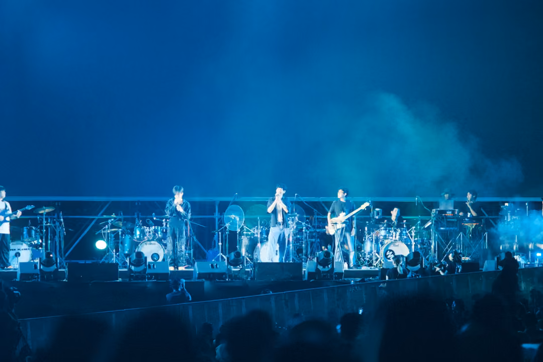 Band on a stage swallowed by blue and white smoke, the singer and guitarists visible at centre and right.