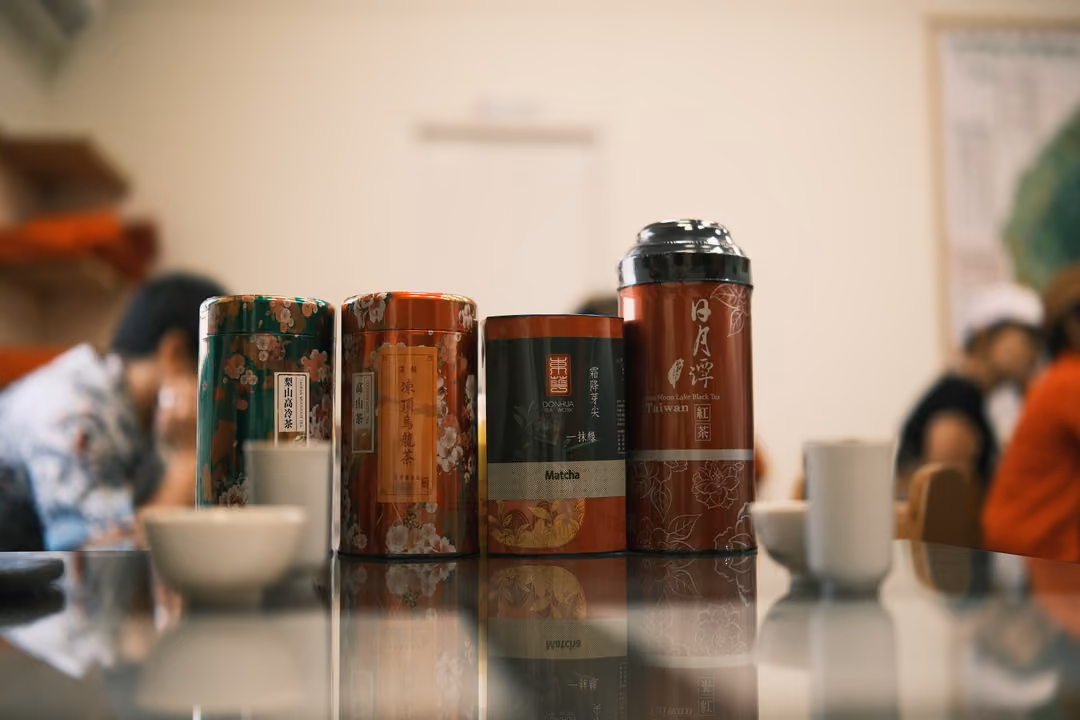Row of four tea tins and white cups on a table, guests blurred in the background of a tasting room
