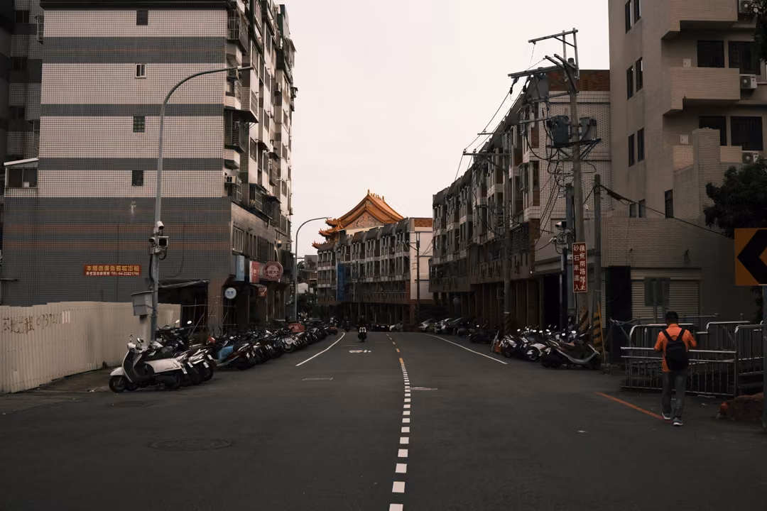 Empty city street with dashed centre line, parked scooters and apartment blocks leading to an ornate tiled roof