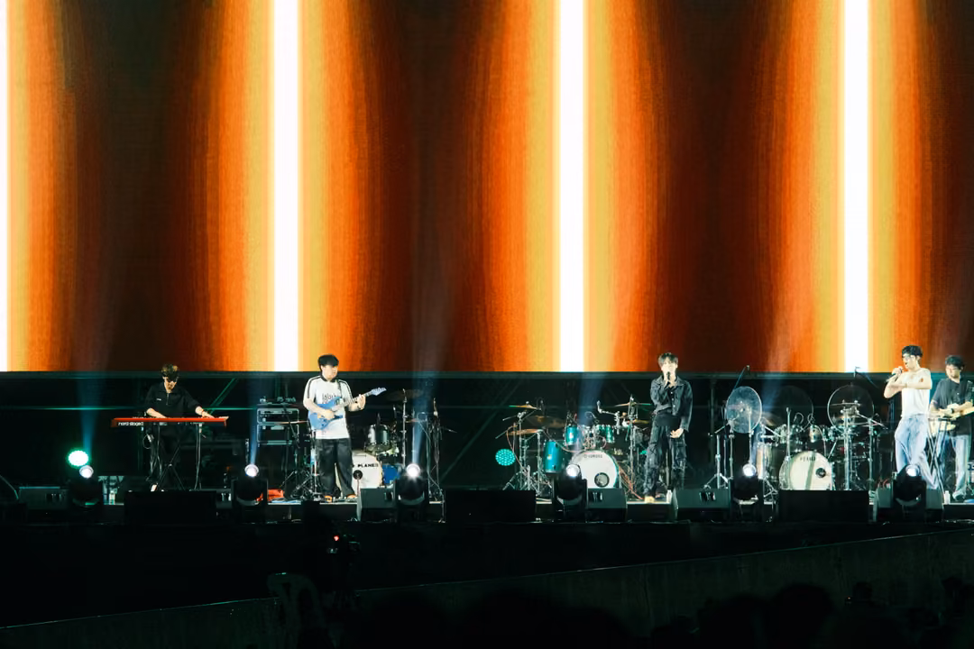 Musicians on stage in front of a screen filled with glowing orange and white vertical stripes.