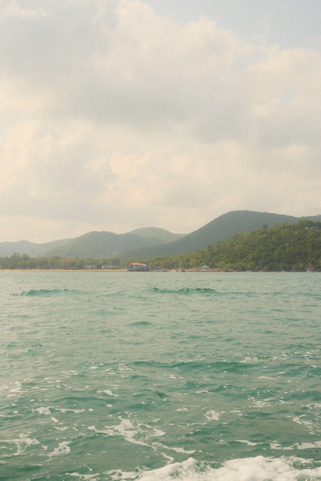 Green hills and a low headland across turquoise sea, with white clouds above.