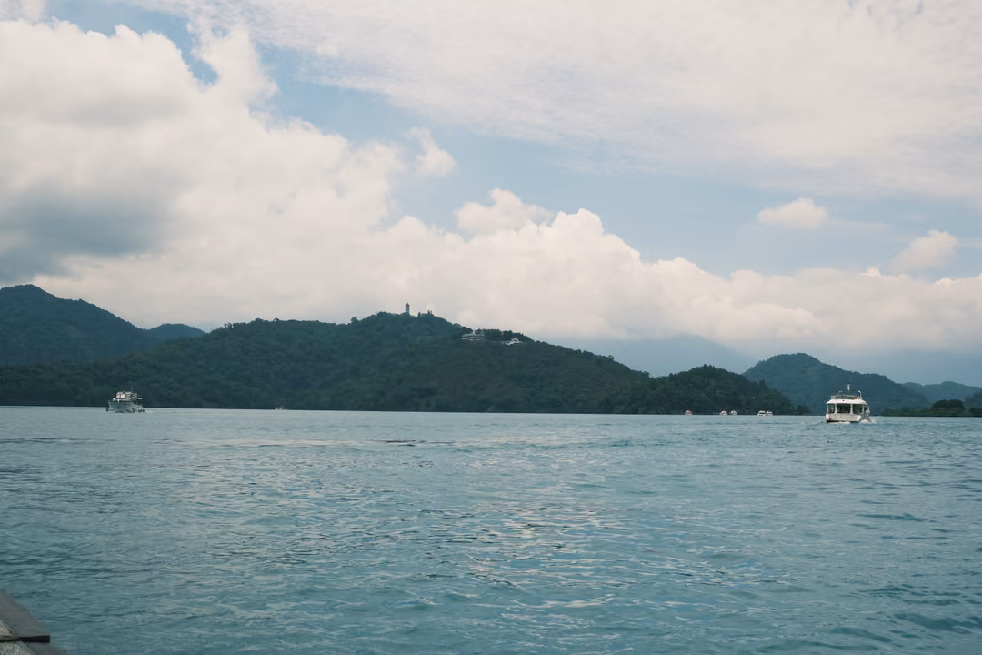 Wide calm lake under scattered clouds with low forested hills and two distant boats