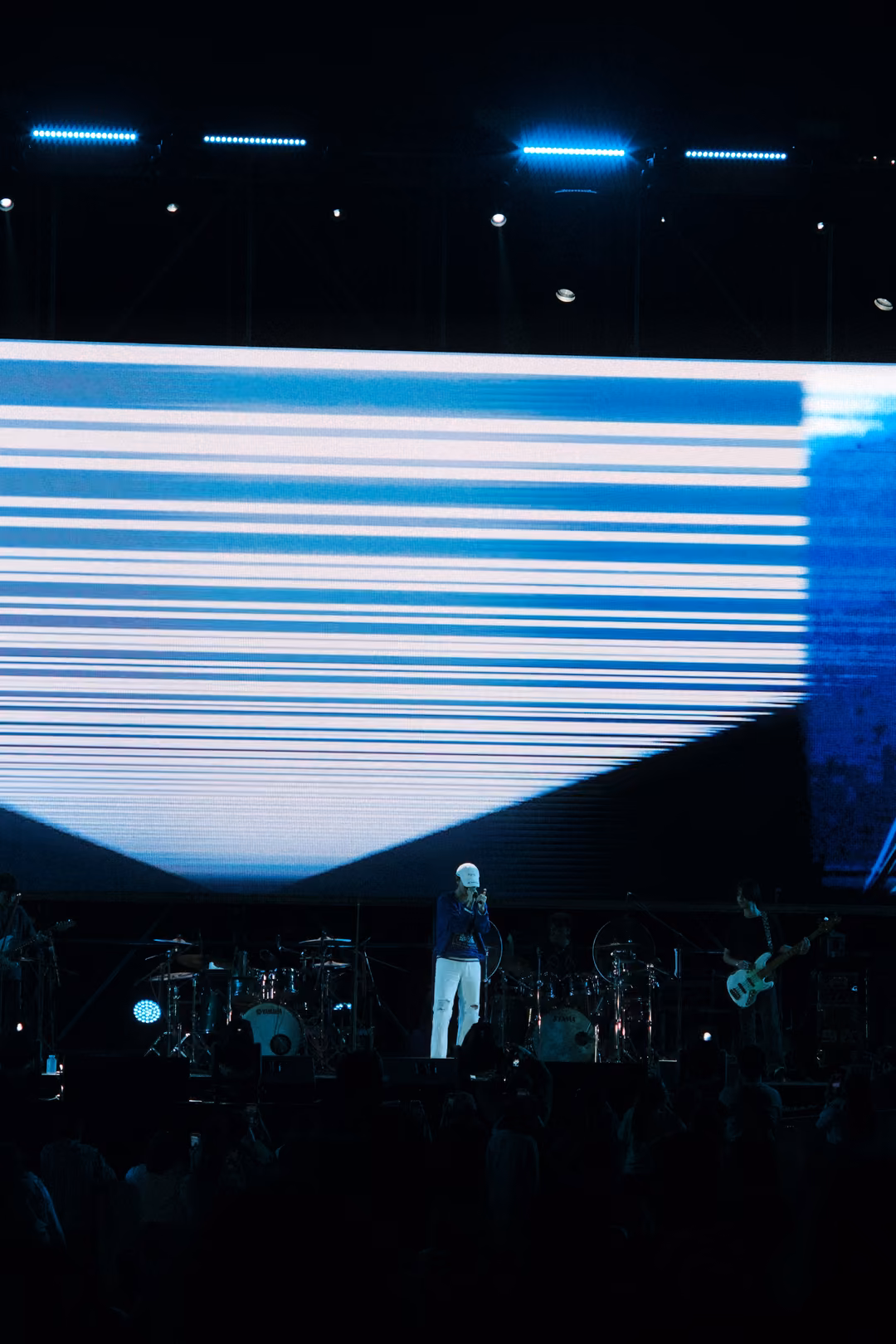 Vertical view of a screen of white horizontal streaks narrowing to a V, the singer standing on the dark stage below.