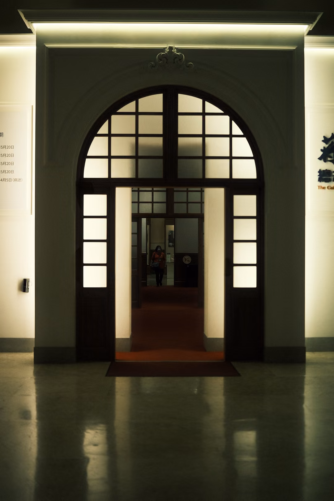 Arched doorway with a fanlight of square panes and double doors, a red carpet runner in a polished hall