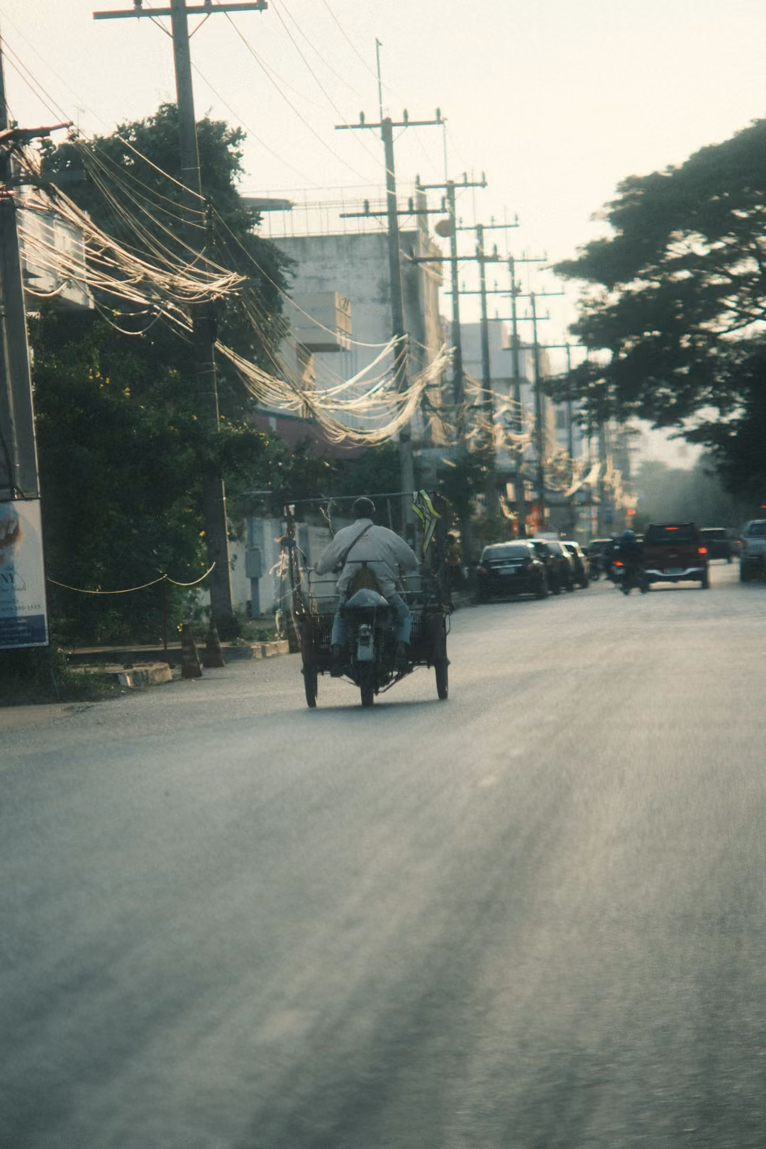 A rider on a three-wheeled motorbike cart heads down a hazy road lined with power poles and looping cables.