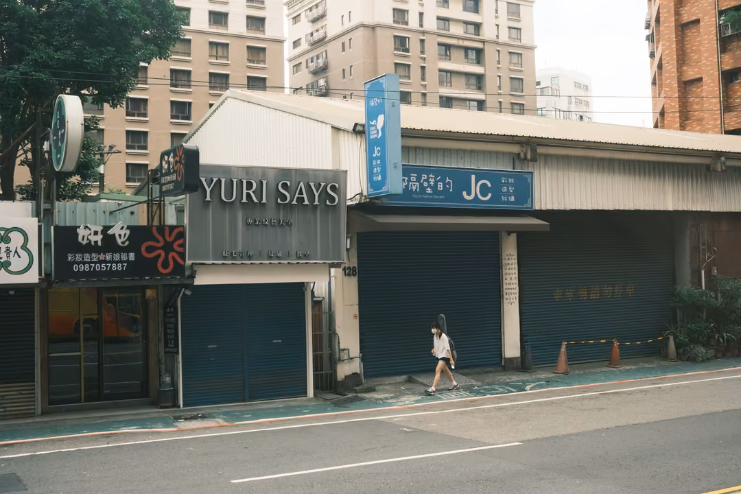 Closer view of YURI SAYS shop and neighbouring signs, blue shutters closed, a pedestrian walking past