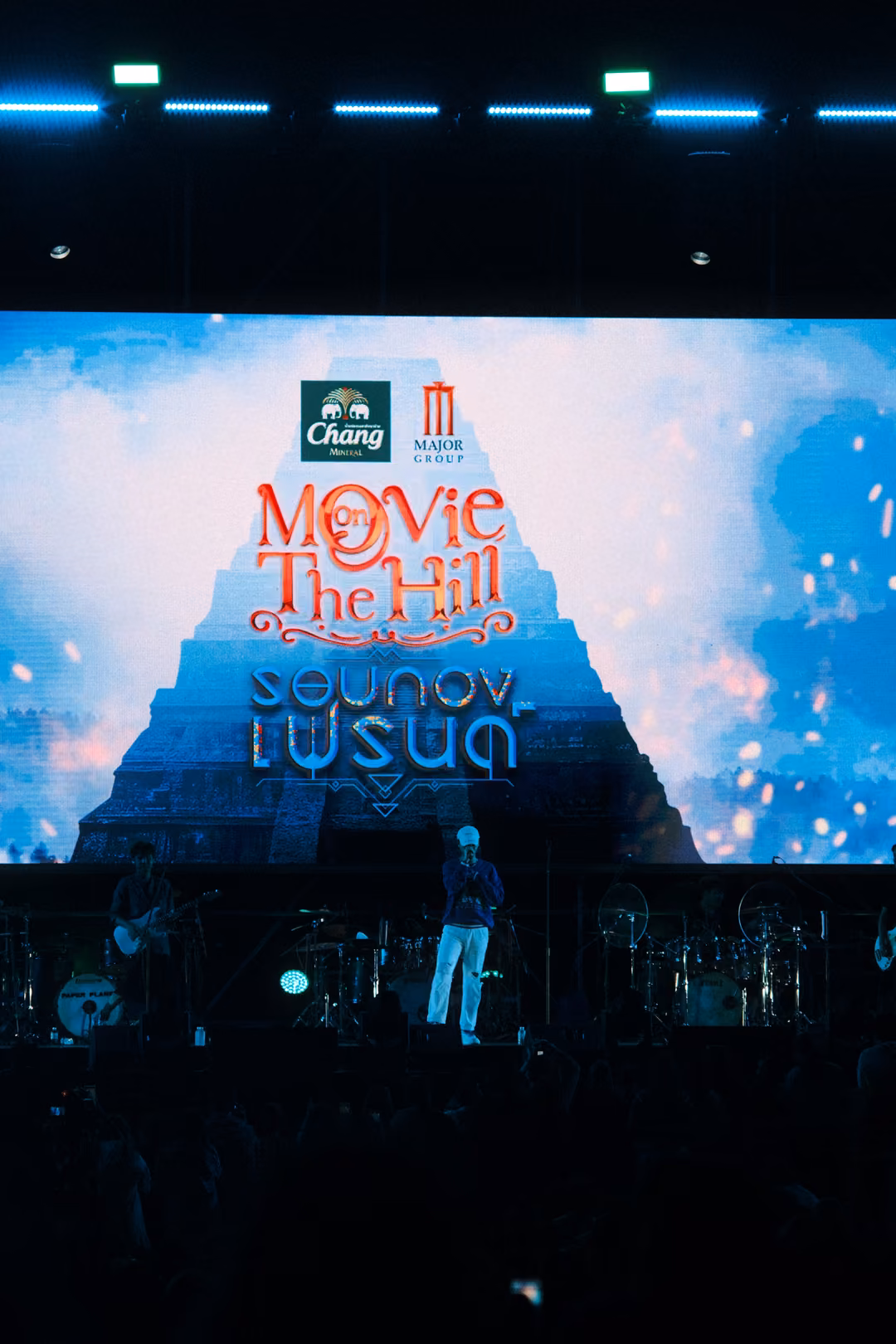 Vertical view of a screen with the Movie on The Hill title over a pyramid, the singer standing alone on stage below.