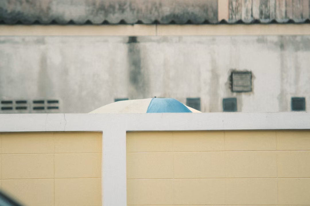 Pale wall with a blue-and-white umbrella top peeking above a yellow-tiled wall