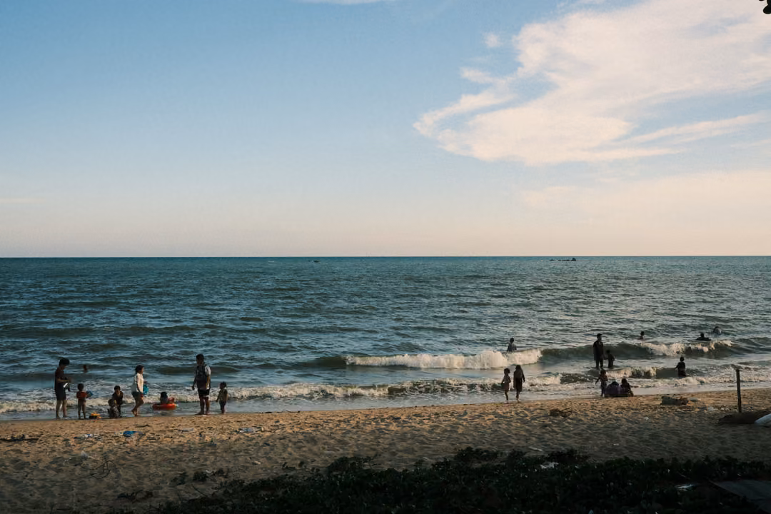 Families on a sandy beach and in the shallow surf, breaking waves and a sky with soft white clouds