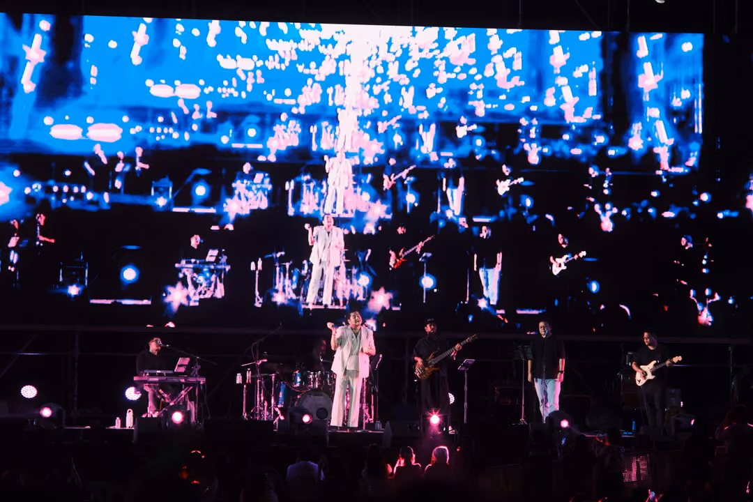 Big screen showing a wide shot of the band surrounded by blue and white sparkles, the same band lit on stage below