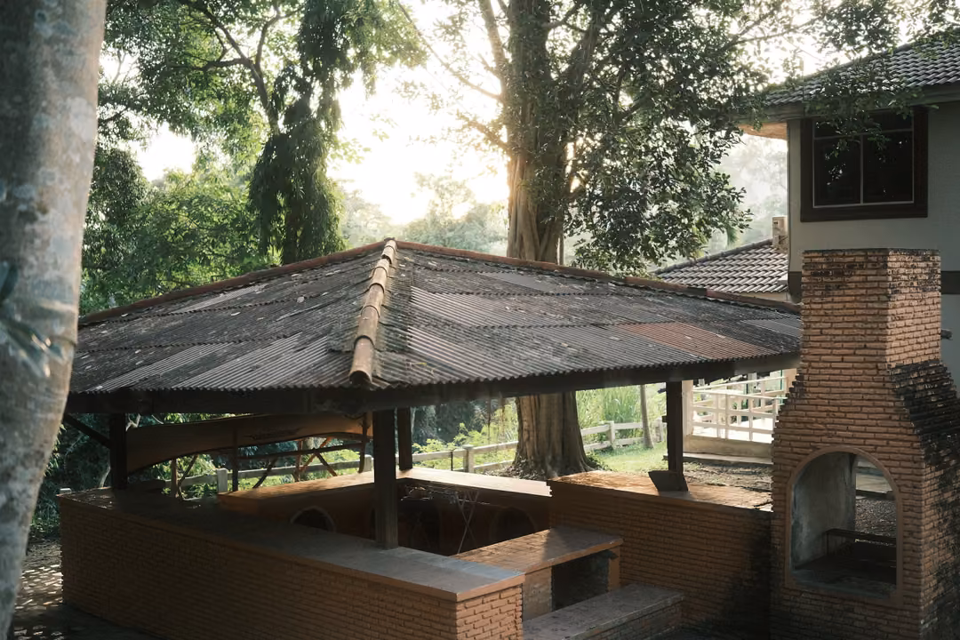 Brick pavilion with a corrugated roof, brick benches and a brick oven, trees behind