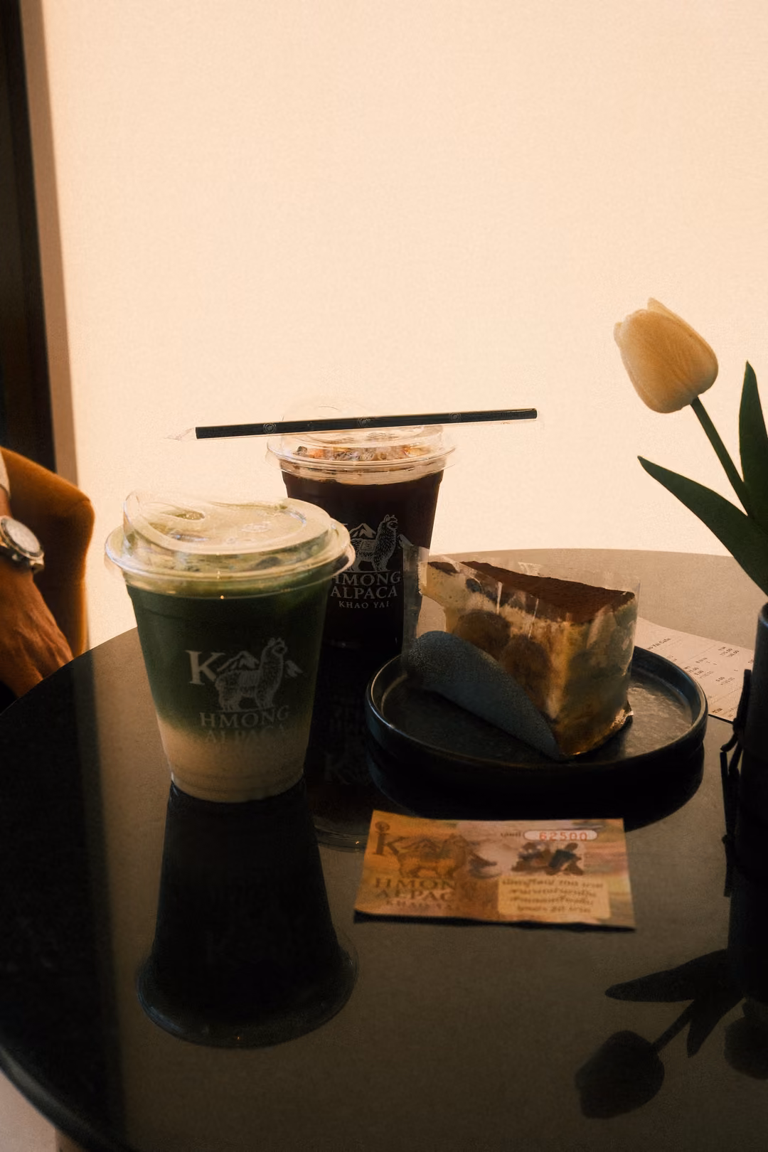 The café table with drinks, cake and tulip, now with a small printed card and a hand at the left edge.