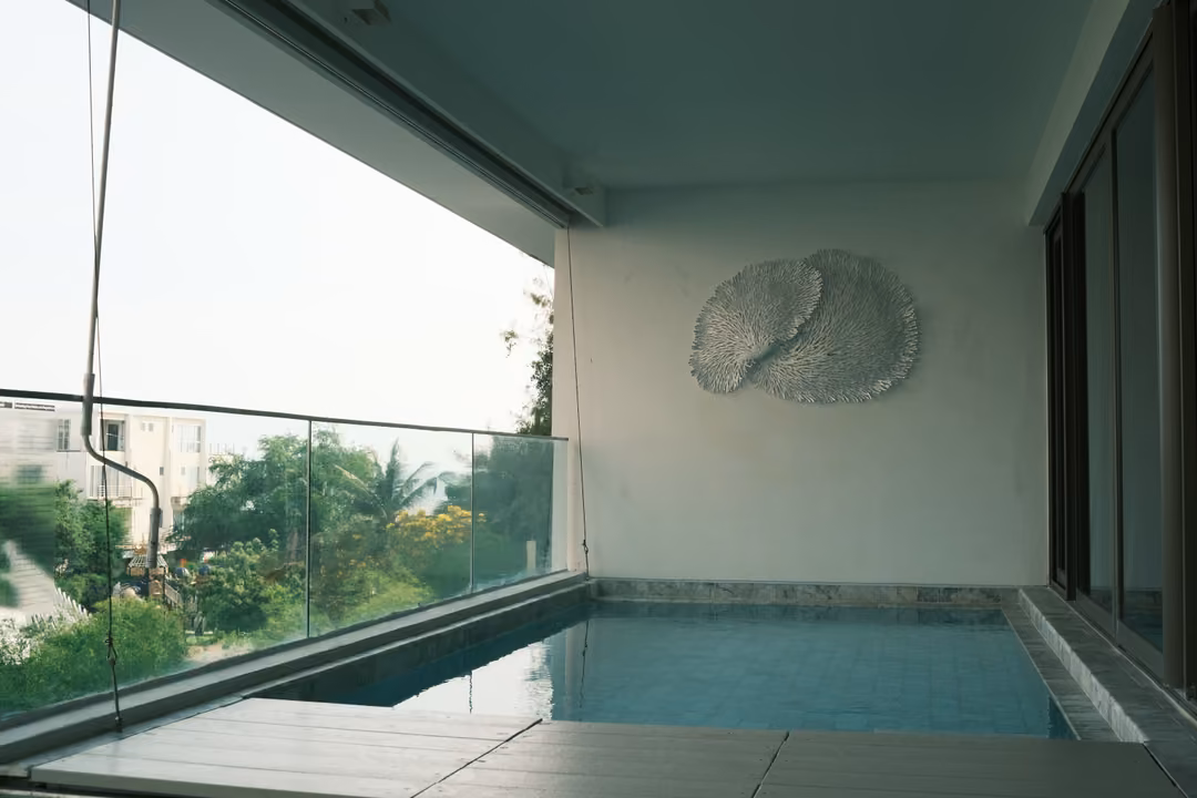 A covered balcony with a narrow plunge pool, glass railing and a white coral-like wall sculpture