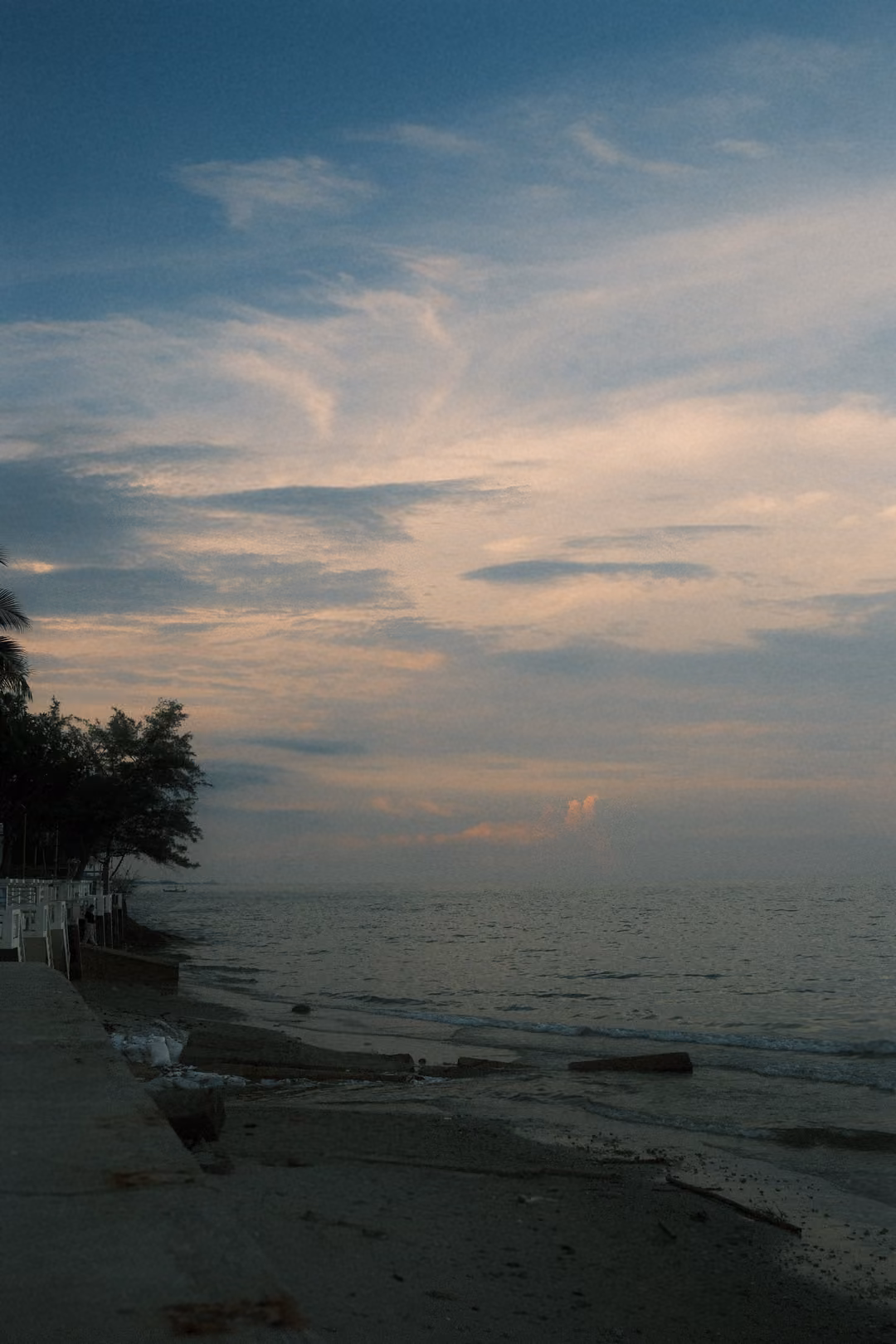 Pastel evening sky over the sea, an eroded sandy shore and concrete wall in the foreground