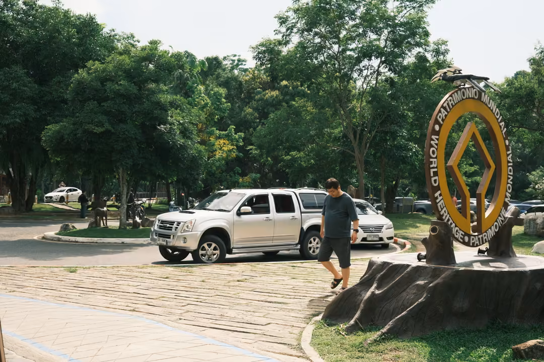 A man walking past a round emblem sign reading World Heritage on a stump, a pickup truck behind