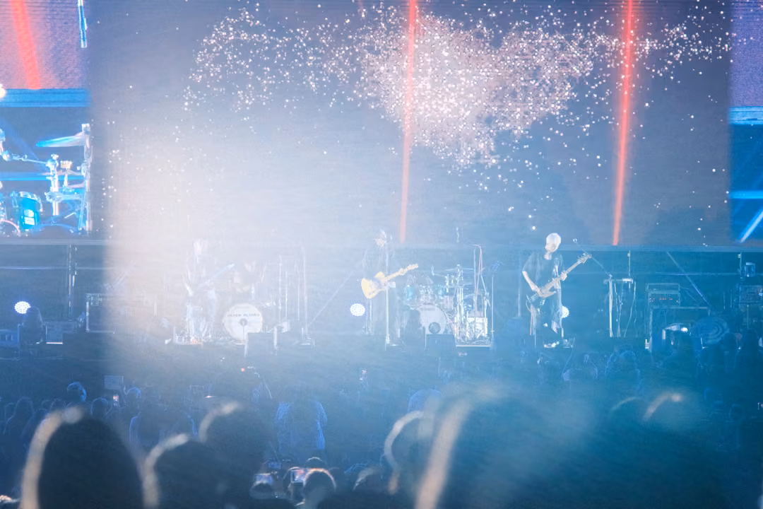 Hazy blue stage washed in light, glittering particles on the screen and red light beams, heads of the crowd in soft focus