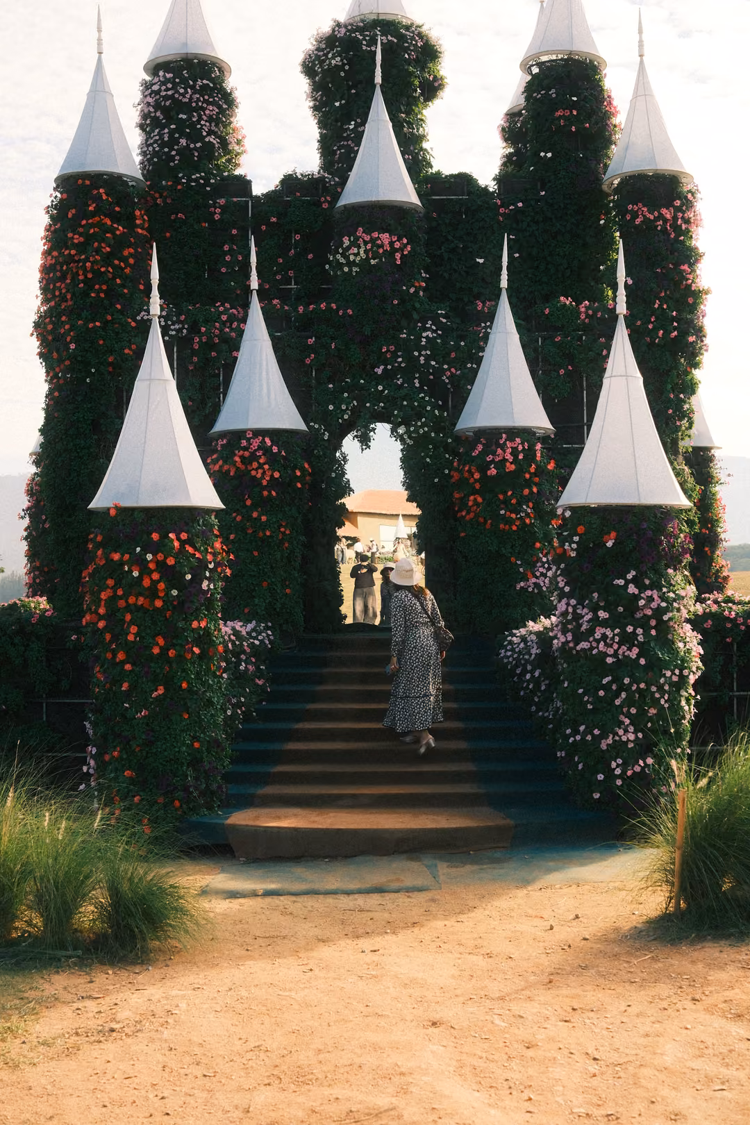 Close view of the castle's flower-covered towers and archway, a person in a patterned dress on the steps.