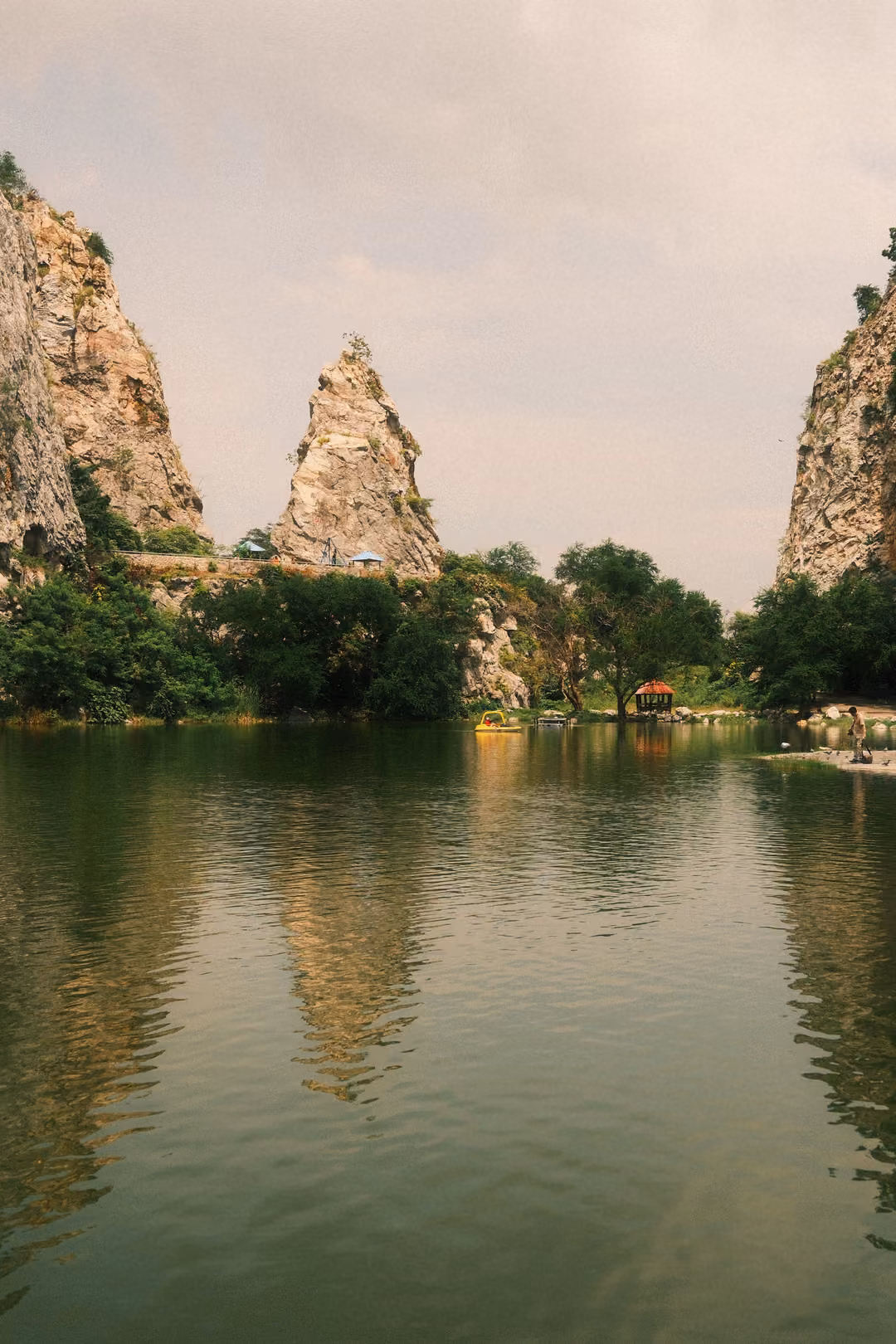 Pointed limestone spire between two cliffs mirrored in a still green lake, vertical frame