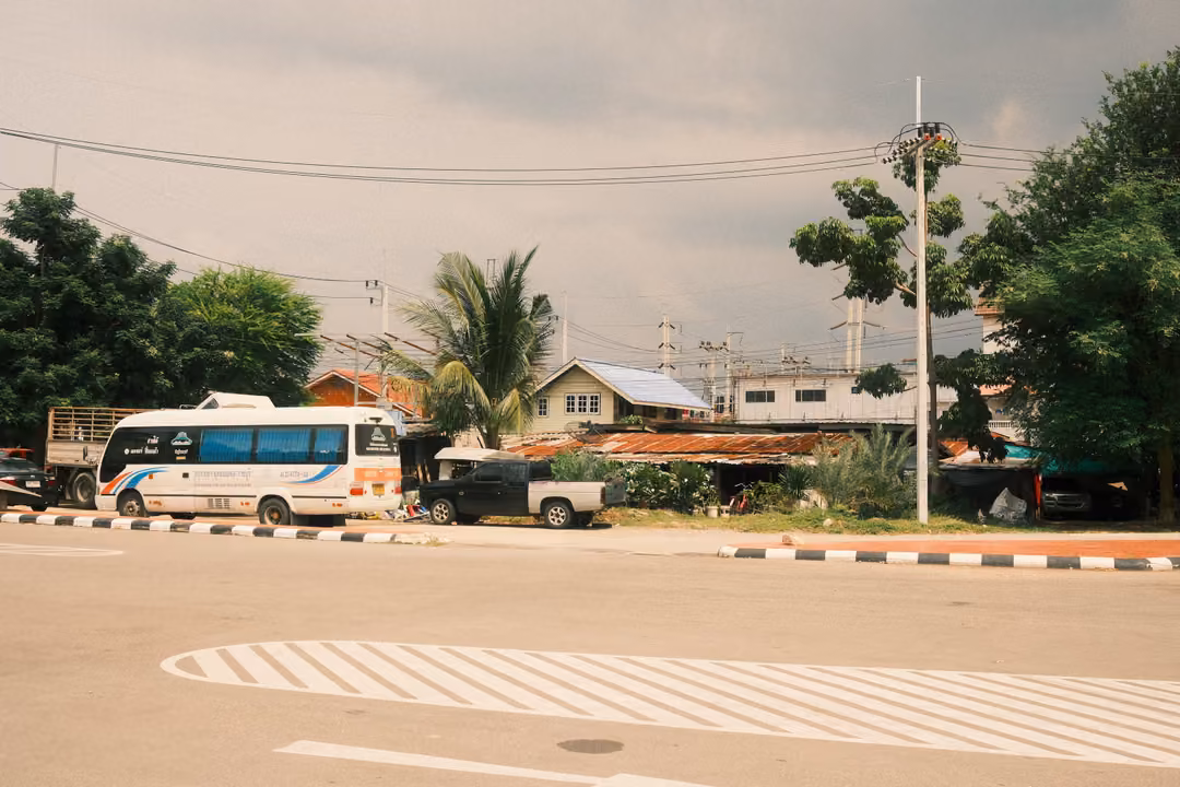 Road junction with a white bus parked under an overcast sky, striped road markings, trees and power lines