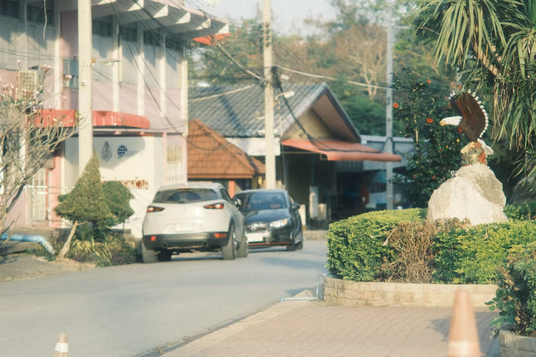 A driveway with a white SUV and a dark car beside hedges and a rock topped by an eagle sculpture.