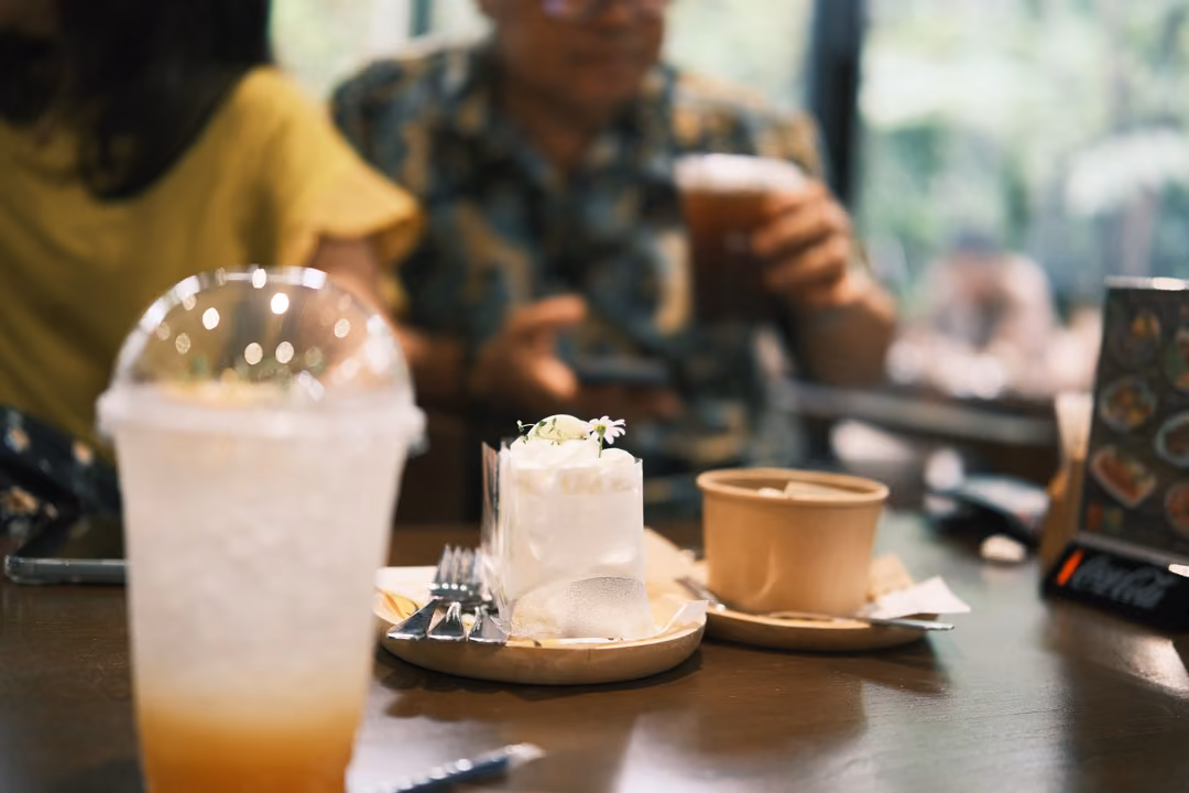 On a café table: an iced orange-layered drink in a domed cup, a slice of white cake and a small cup.