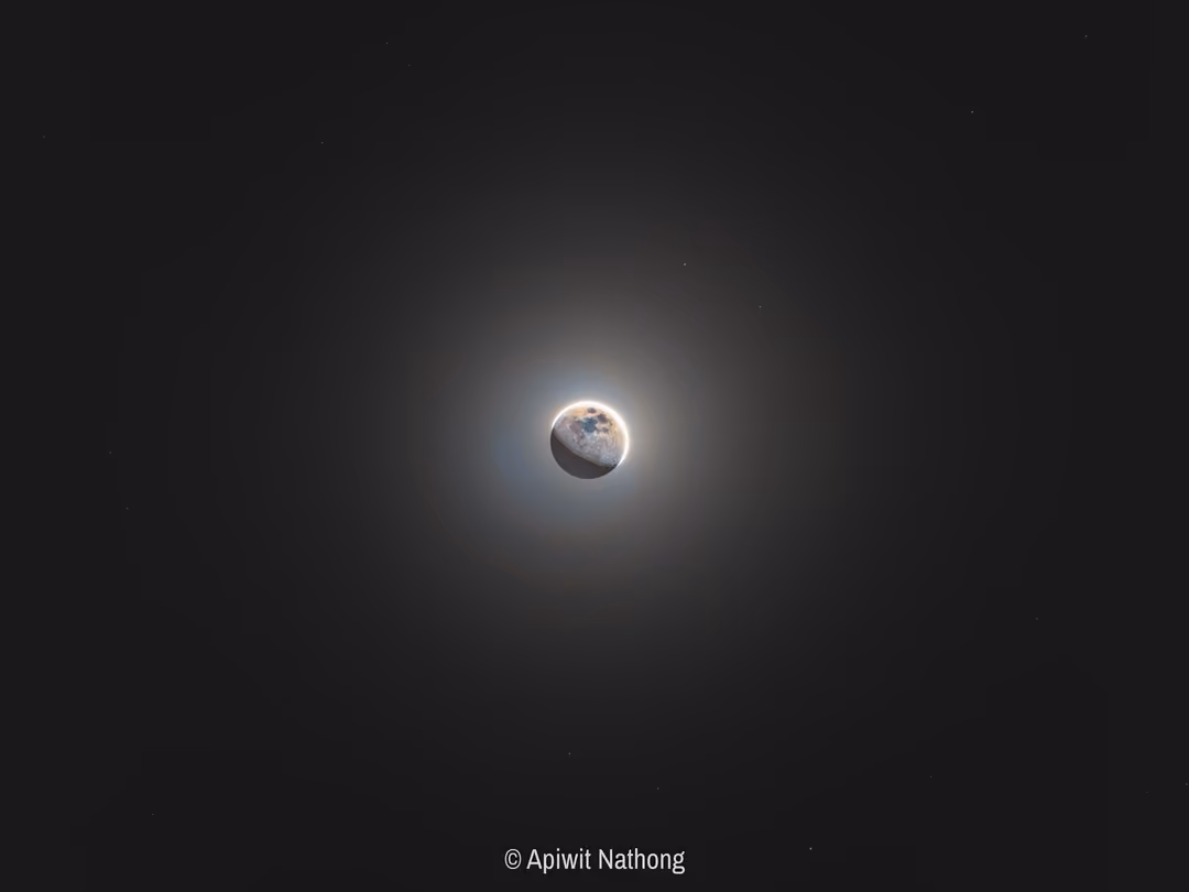 A small moon inside a large soft halo of light against a dark grey sky