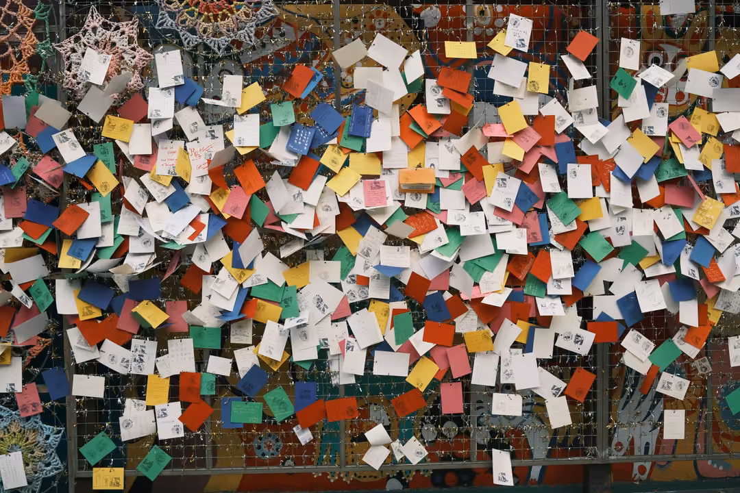 Mesh wall covered in hundreds of small colourful paper notes and cards
