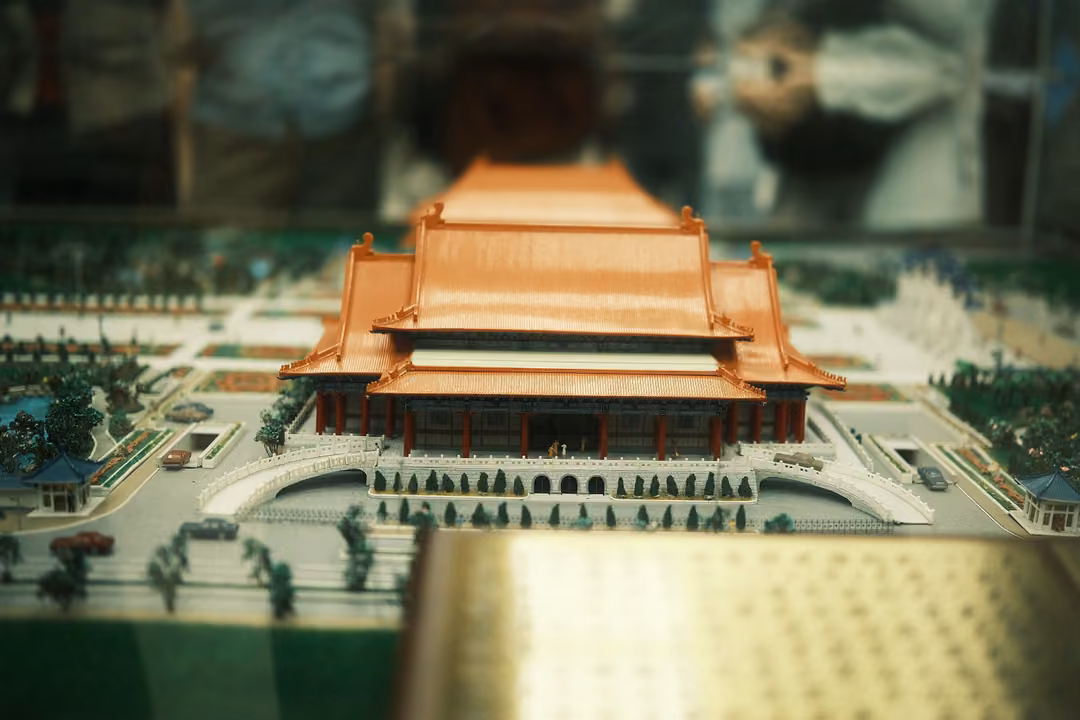 Scale model of a large orange-roofed hall with gardens and gates under glass, reflections of visitors above