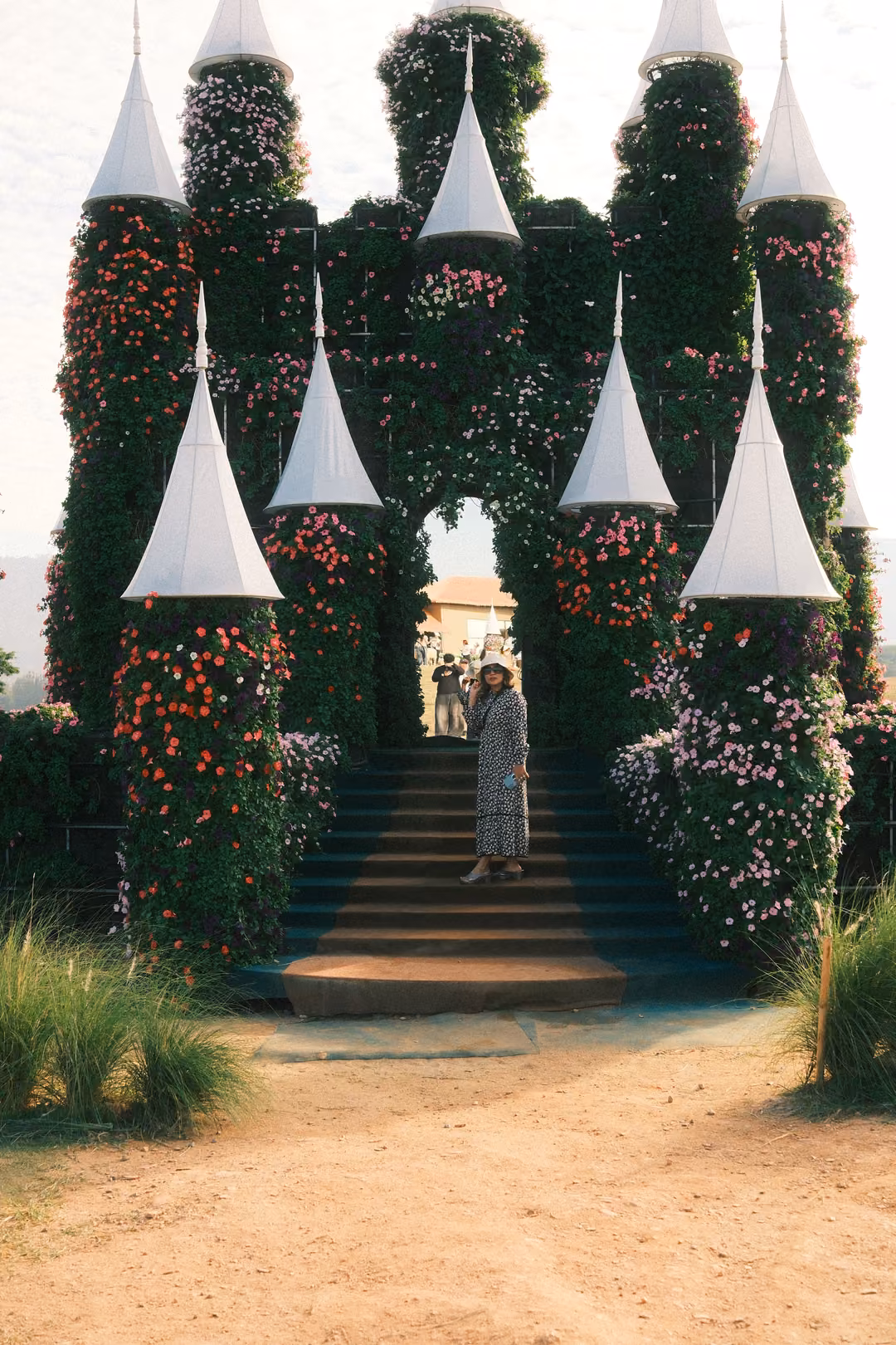 Upright view of the flower-covered archway and steps, a person in a patterned dress standing on them.