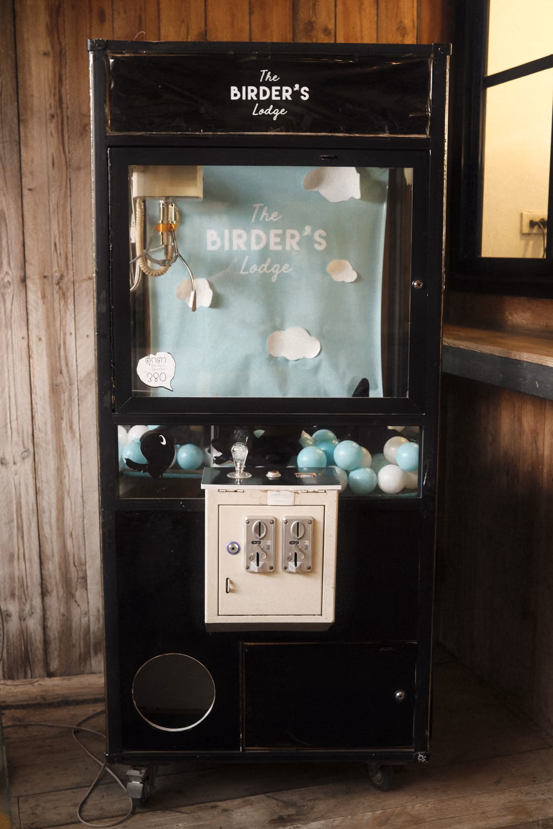 A black claw machine full of pale blue balls standing against a wooden wall, a cloud backdrop inside