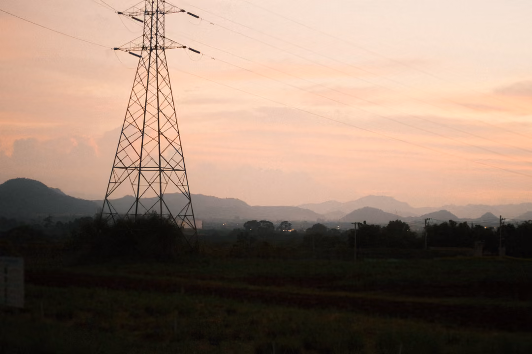 Electricity pylon centered against a pink sunset sky, mountains and dark fields below