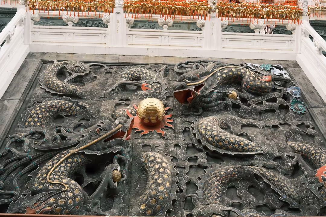 Wide view of a dark stone dragon relief set into a courtyard, ringed by white balustrades and red eaves