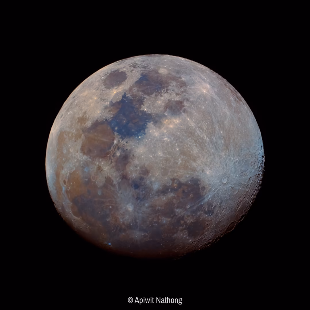 A nearly full moon with enhanced colours showing blue and brown tones across its seas and craters