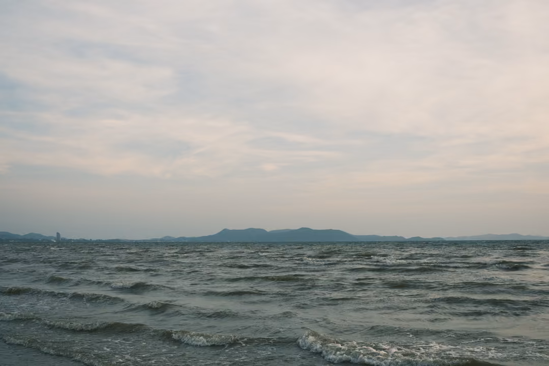 Choppy grey sea stretching to a low line of distant hills under a soft cloudy sky