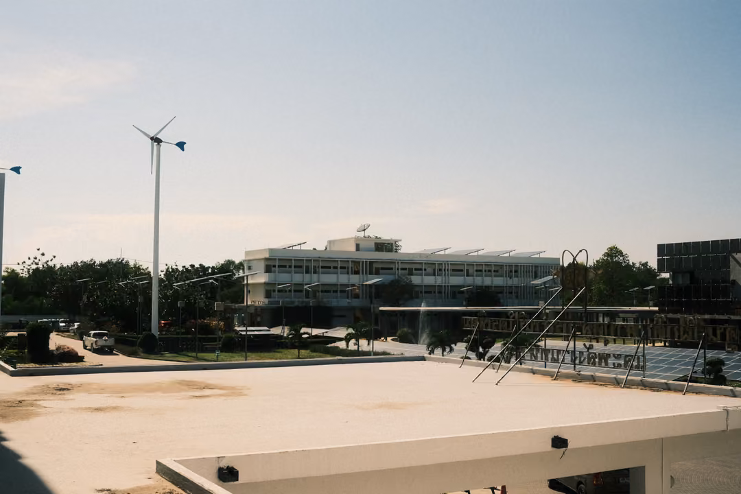 Rooftop view across a sandy flat roof to a modern building, a small wind turbine and solar panels