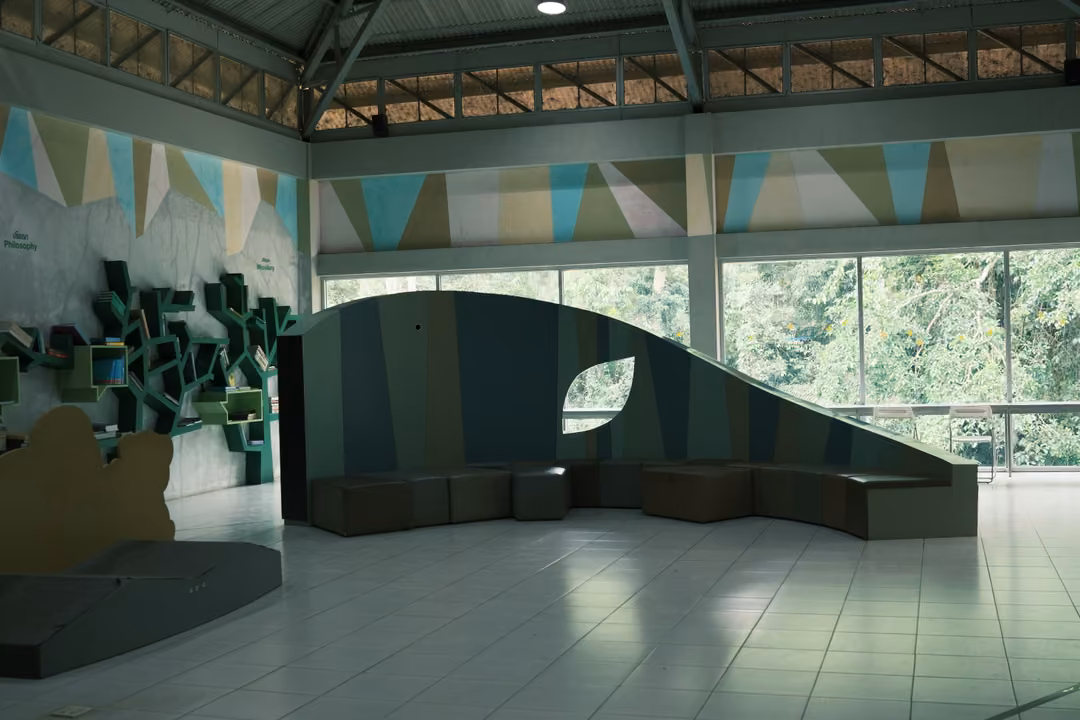 A wide hall with a curved striped wall, bench seating, a green display shelf and bright windows