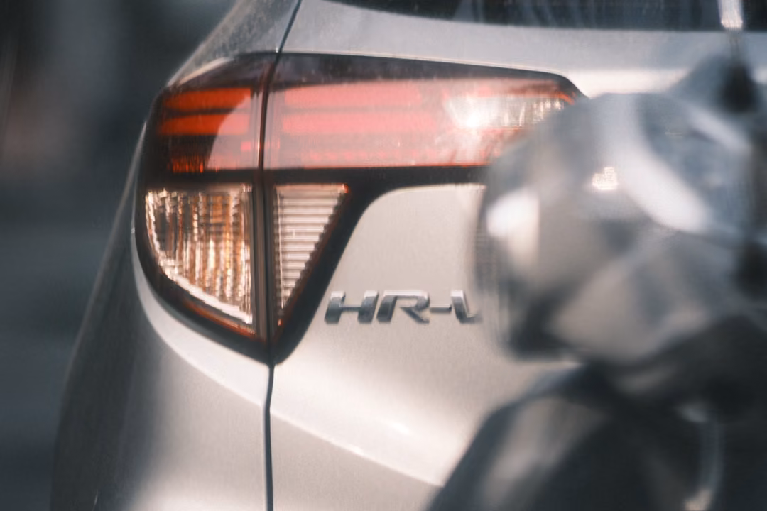 The same silver car's tail light and badge, slightly tighter, with a blurred grey shape in front.