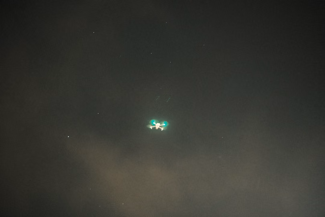 Small green light hovering in a dark hazy night sky