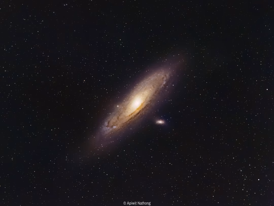 The Andromeda Galaxy, a large tilted spiral with a bright core and dust lanes, surrounded by stars