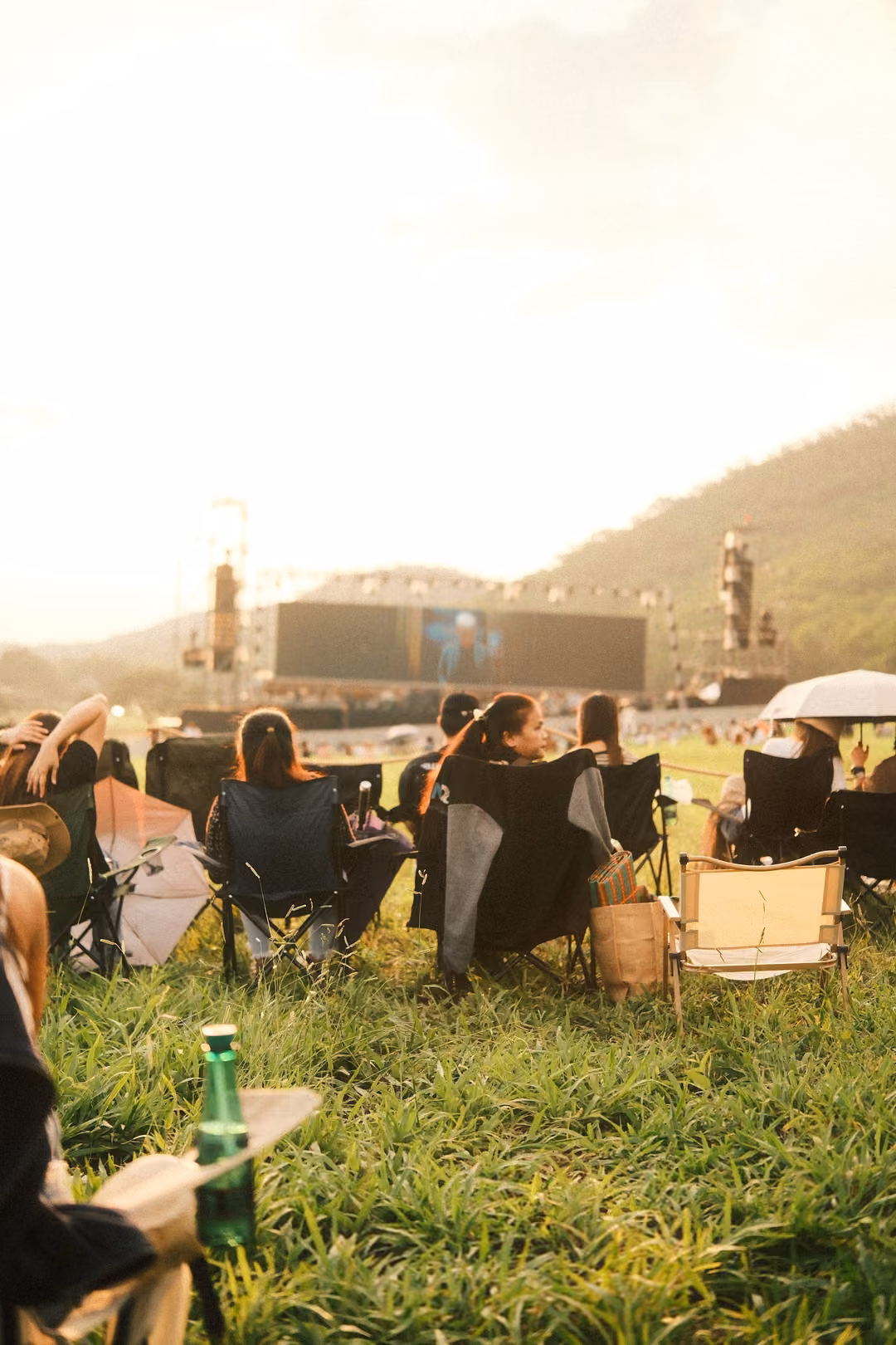 Upright view of chairs on a grassy slope facing a big screen, a green bottle in the foreground.