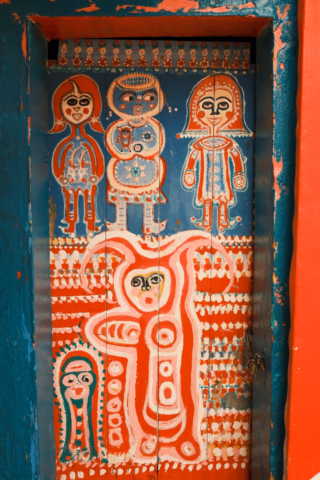 Door painted red and blue with whimsical figures with large eyes and patterned bodies
