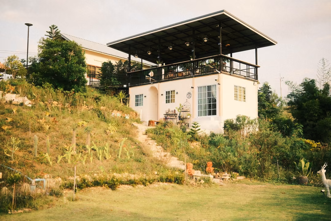 A white house with an open roof terrace on a planted slope, a white deer figure on the lawn in front.