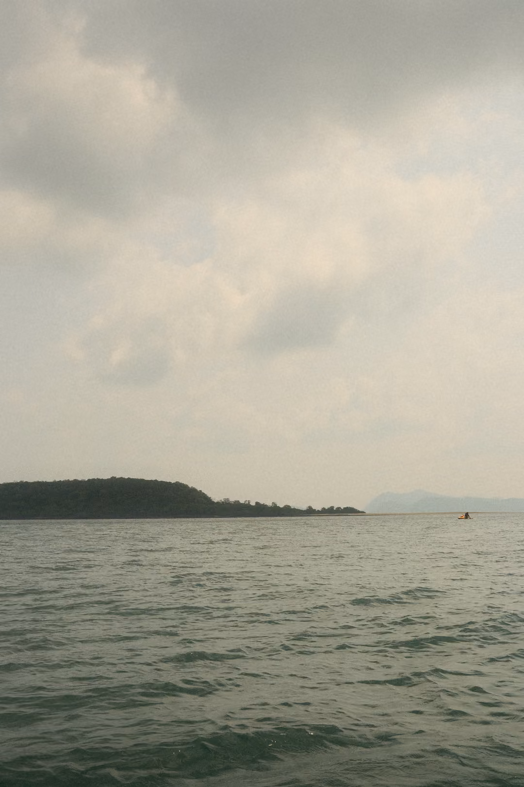 A dark island low on the horizon under a heavy, overcast sky above a grey sea.