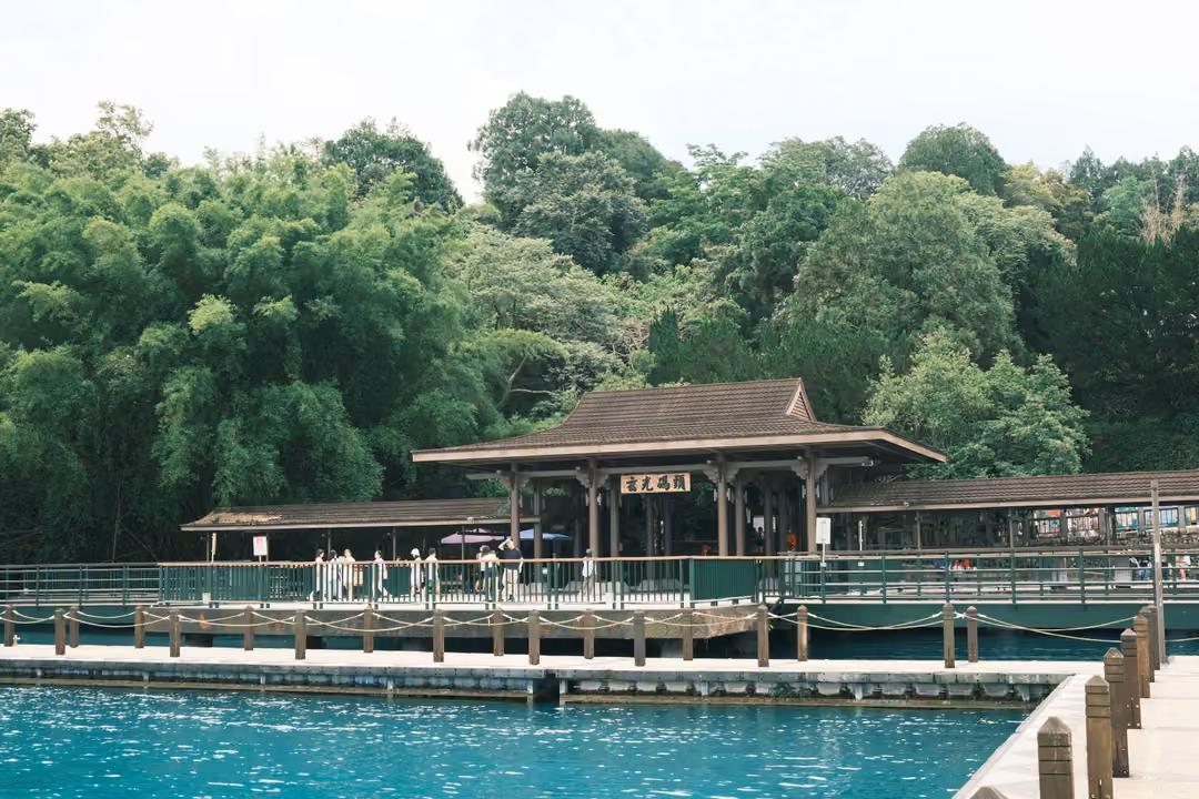 Wooden pier pavilion with a dark tiled roof beside turquoise water, dense bamboo and trees behind