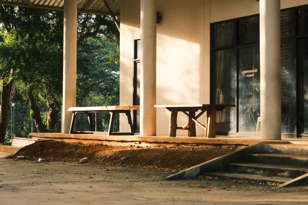 The same veranda with columns, wooden tables and steps, the shadows slightly shifted in golden light.